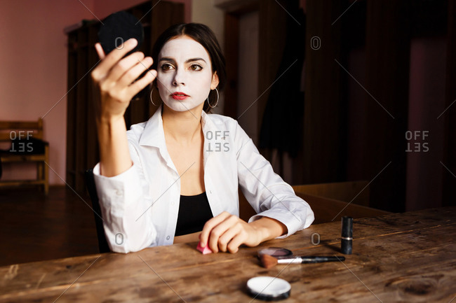 A portrait of an actress woman in a shirt who is sitting on the chair and doing professional theatrical makeup for the stage