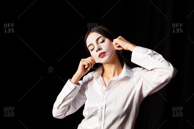 A portrait of an actress woman in a shirt and with done theatrical makeup who is posing like a mime and pull her face skin
