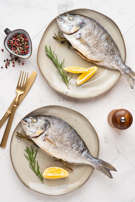 Overhead view of cooked dorado fish served on plate with lemons and herbs