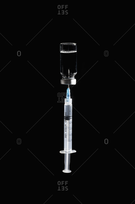 Syringe in COVID-19 vaccine vial on black background