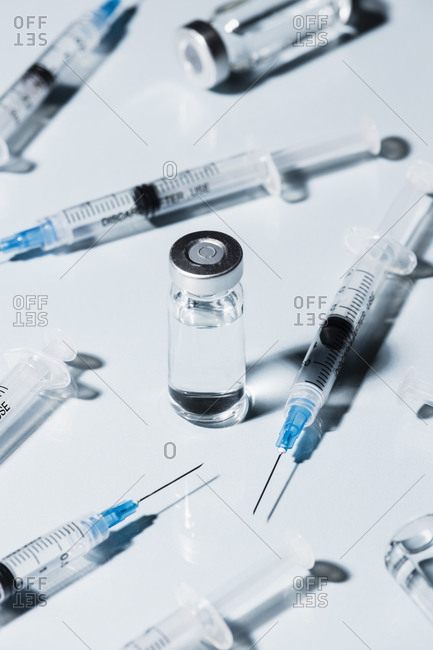 Syringes around COVID-19 vaccine vial on white background