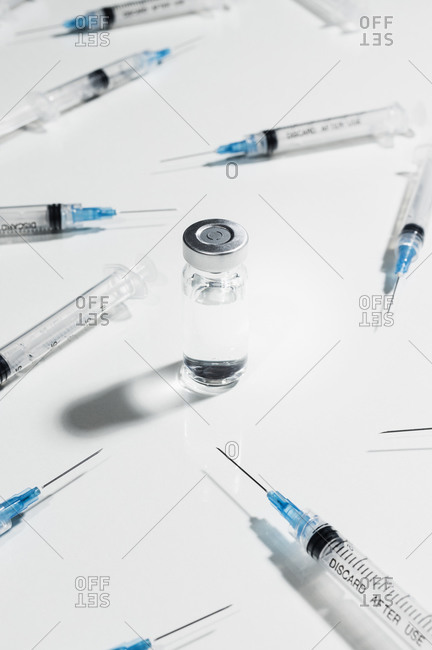 Syringes surrounding COVID-19 vaccine vial on white background