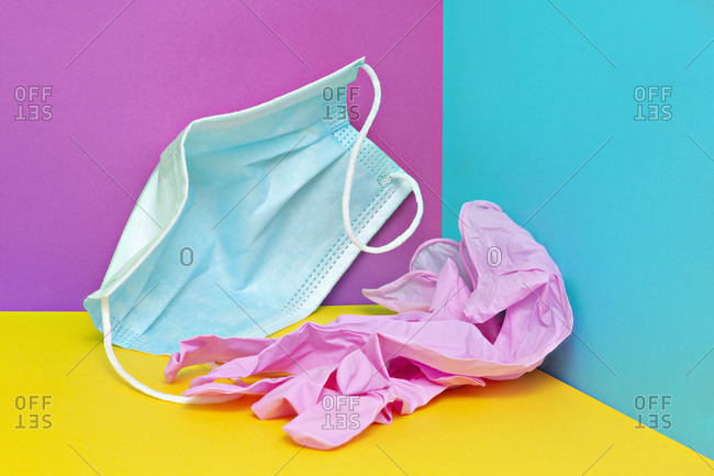 Crumpled face mask and plastic gloves on colorful background