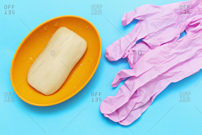 Bar soap and pink protective gloves on blue background