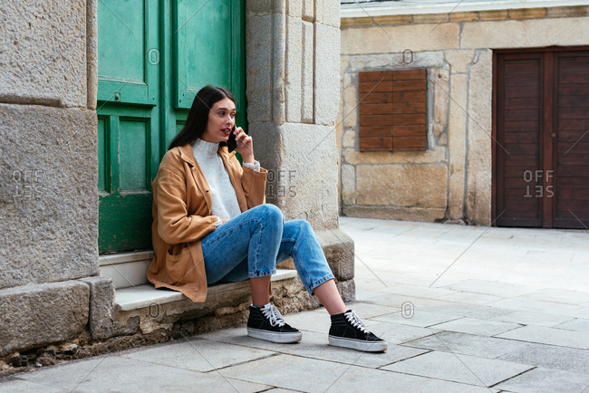 Young beautiful woman sitting outdoors and talking on phone