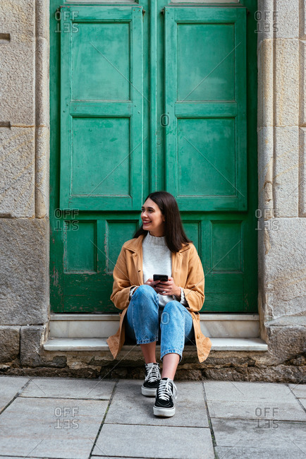 Young stylish woman sitting outdoors and using a smartphone