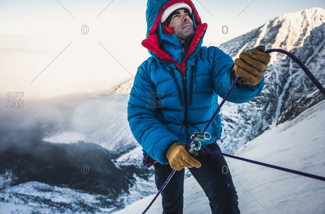 Male climber belays his lead climber during a cold winter alpine climb