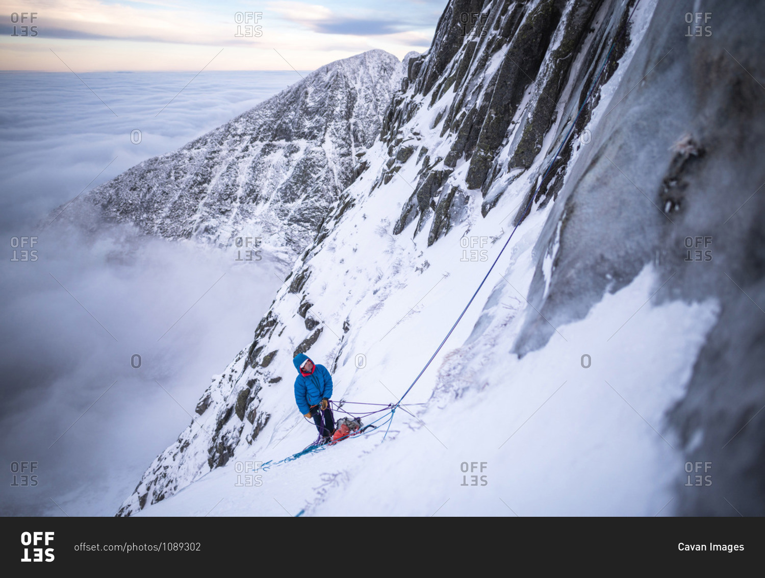 A male climber belaying his lead during a cold winter alpine climb