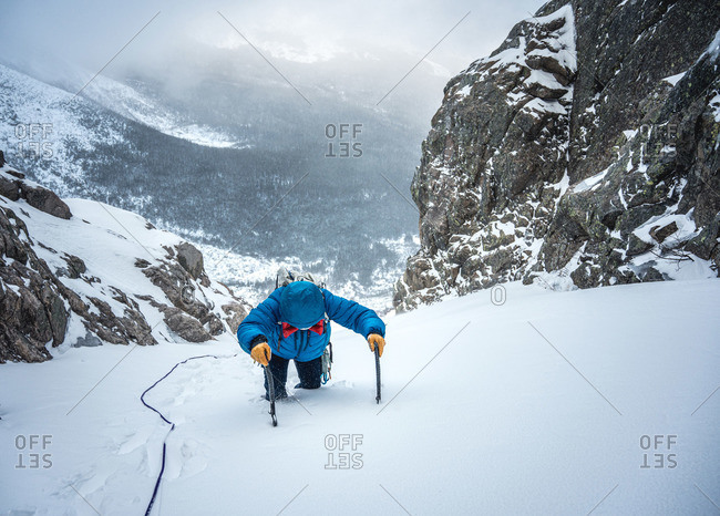 Alpine climber post-holes up a steep section of snow on an ice climb