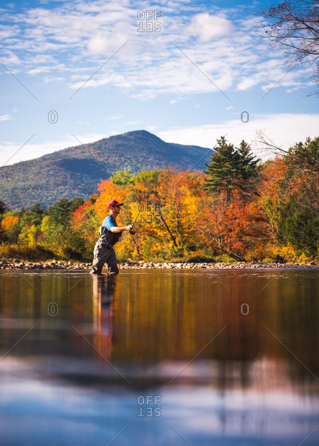Fly-fisherman casting in river with foliage and reflections