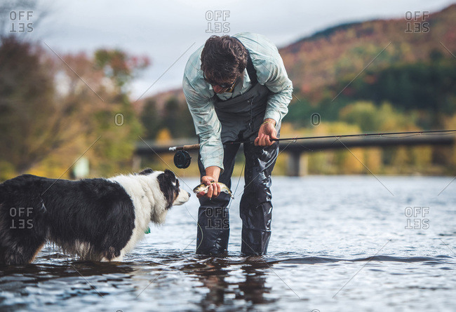 Man holding a small trout while dog sniffs fish