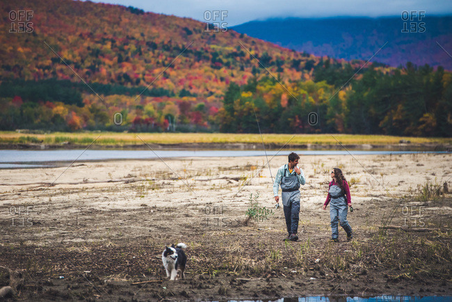 Male and female anglers walk down the shore with dog and foliage