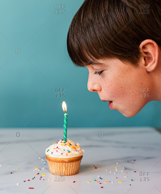 Young boy blowing out a candle on cupcake with frosting and sprinkles.