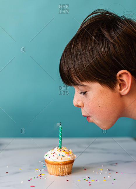 Young boy blowing out a candle on cupcake with frosting and sprinkles.