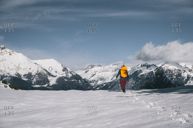 Young man walking in deep snow against snowcapped mountain.