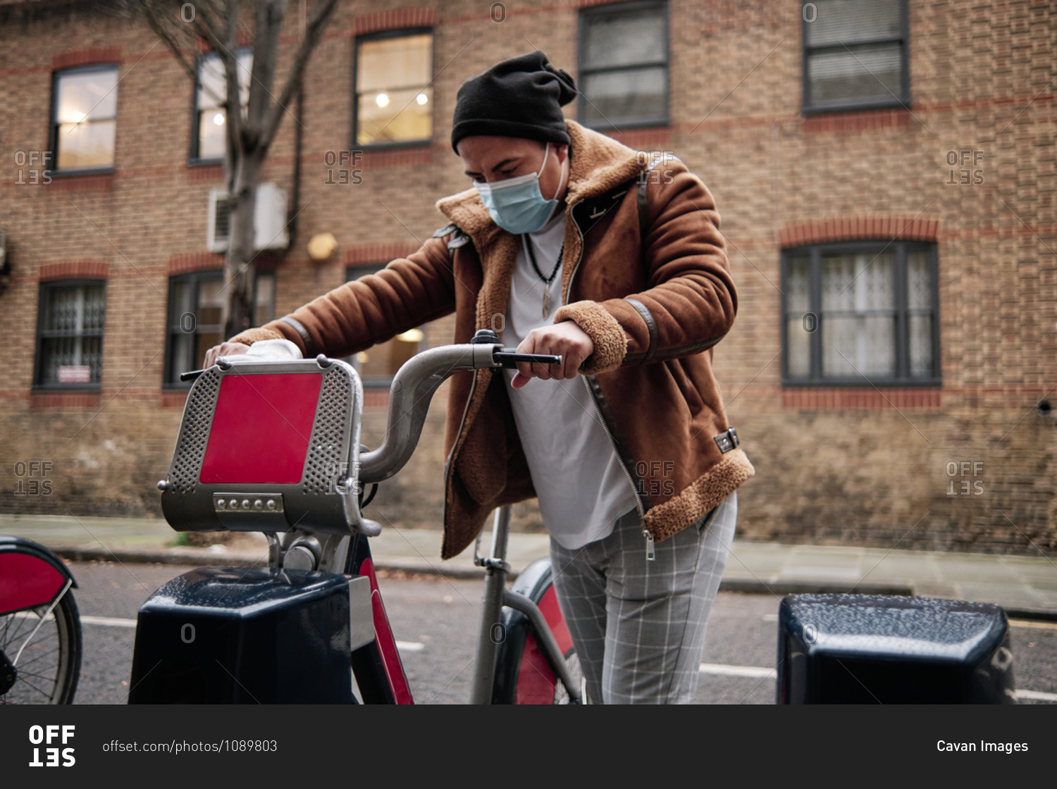 young man wearing a face mask grabbing a bicycle on the\
street stock photo - OFFSET