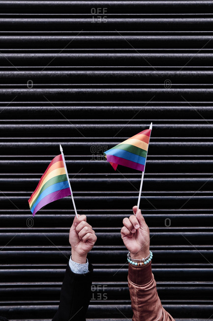 two hands holding pride flags. black background.