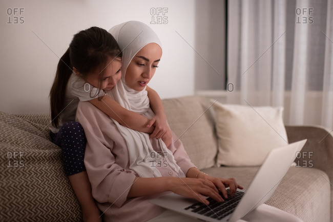 Muslim mother using laptop near daughter