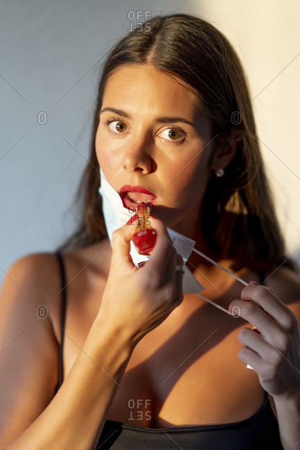 Young woman painting her lips red with a face mask. New normal concept
