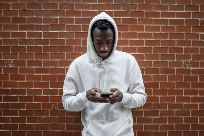 Front shot of African man with serious gesture and hood using smartphone in city