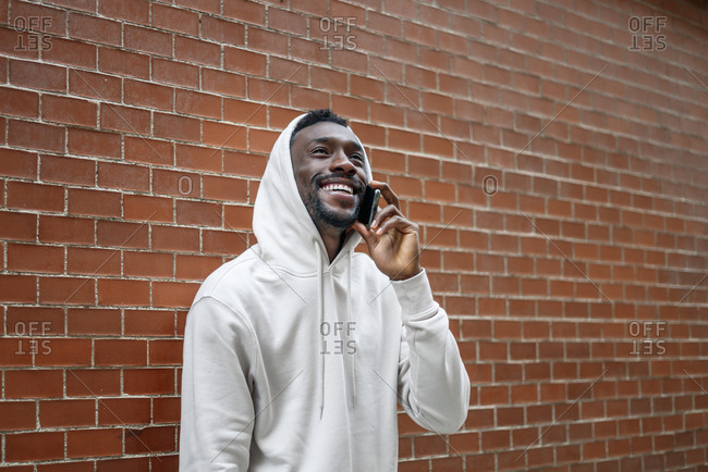 Side shot of African man with happy gesture and hood using smartphone in city