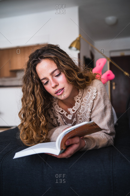 Fascinated young woman reading book on sofa