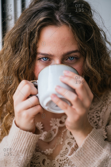 Young female with blue eyes sipping hot drink and looking at camera