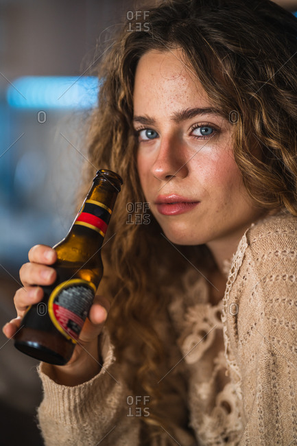 Young woman drinking beer at home and looking at camera