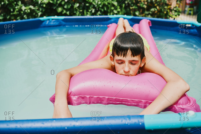 Front view of a blonde boy lying on a pink float resting in a pool.