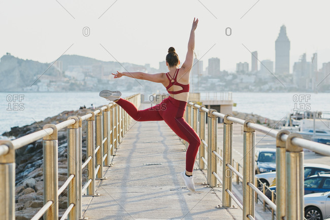 Full body happy young female in white dress jumping with outstretched arms