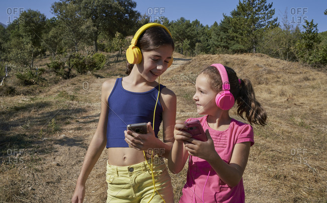 Little girls listening to music and singing with yellow and pink headphones in a garden. music concept