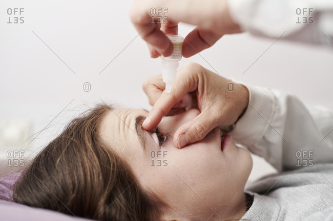 Detail of female doctor smiling and giving eye drops to a little girl in her bed. Home doctor concept