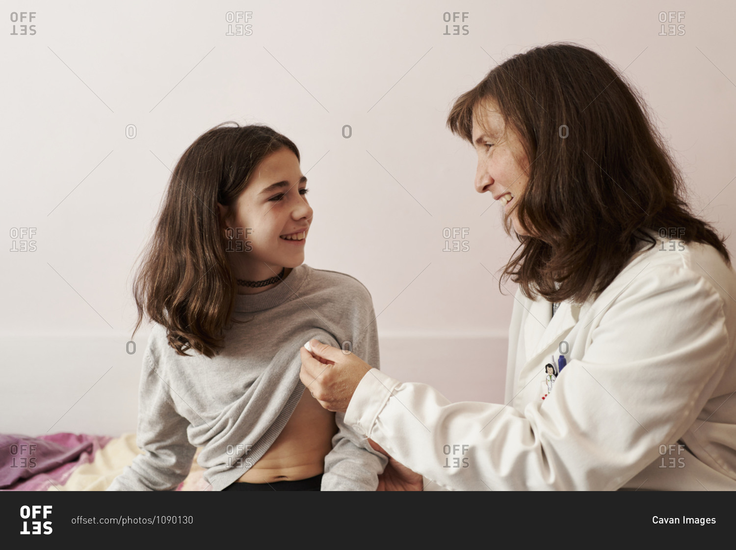 Female doctor teaching the temperature on a thermometer to a girl in her bed. Home doctor concept