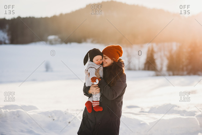 Adorable baby and mom in mountains full of snow on sunny winter day