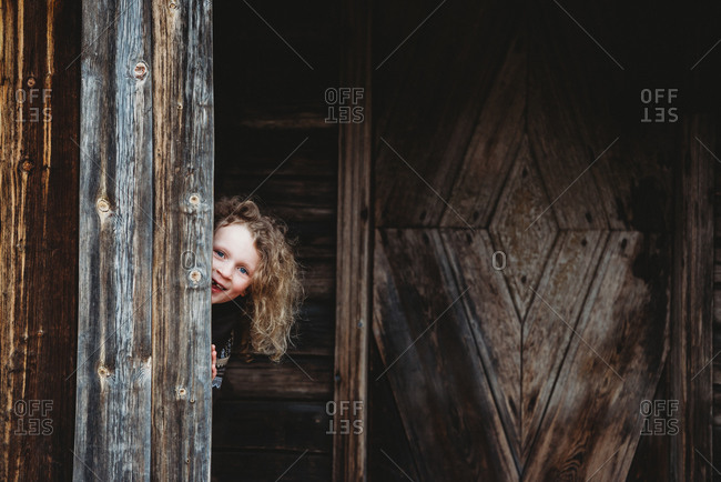 Adorable blonde girl playing hide and seek hiding in old wooden house