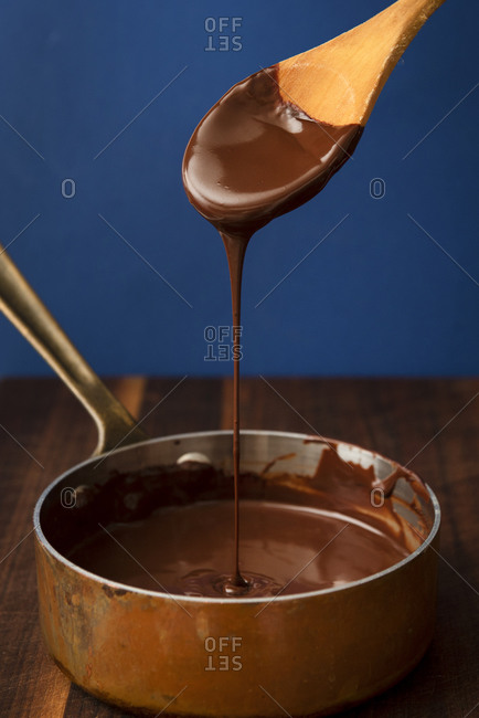 Melted chocolate ganache dripping from wooden spoon into pot