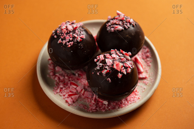 Hot chocolate bombs decorated with crushed candy canes on orange background