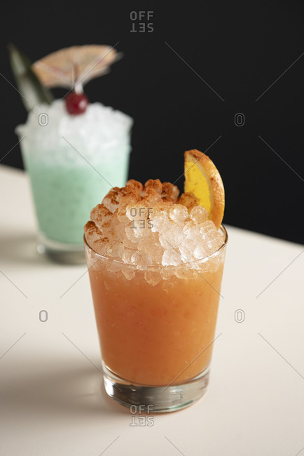 Close up of a pink tiki drink on pebble ice with blue cocktail in background