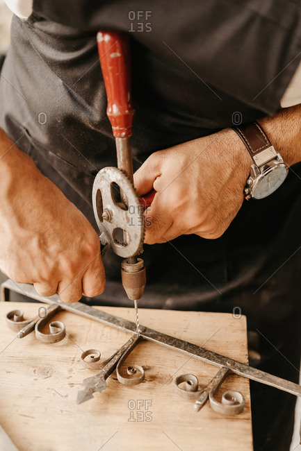 Crop anonymous artisan using old hand drill while working with ornate wooden detail in workshop