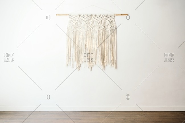 Eco friendly boho style cotton macrame decoration on wooden stick hanging on white wall in light room with minimalist interior