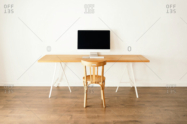 Modern computer placed on wooden table near chair in contemporary light room with minimalist interior