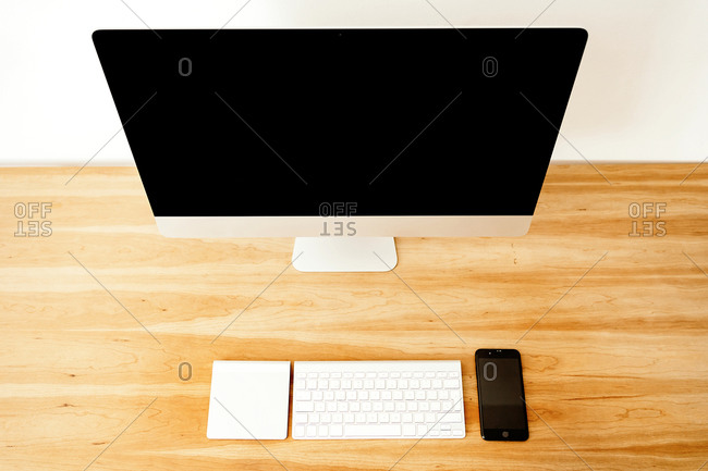 From above of wooden desk with computer monitor and wireless keyboard placed near mobile phone and white notebook at minimalist workplace