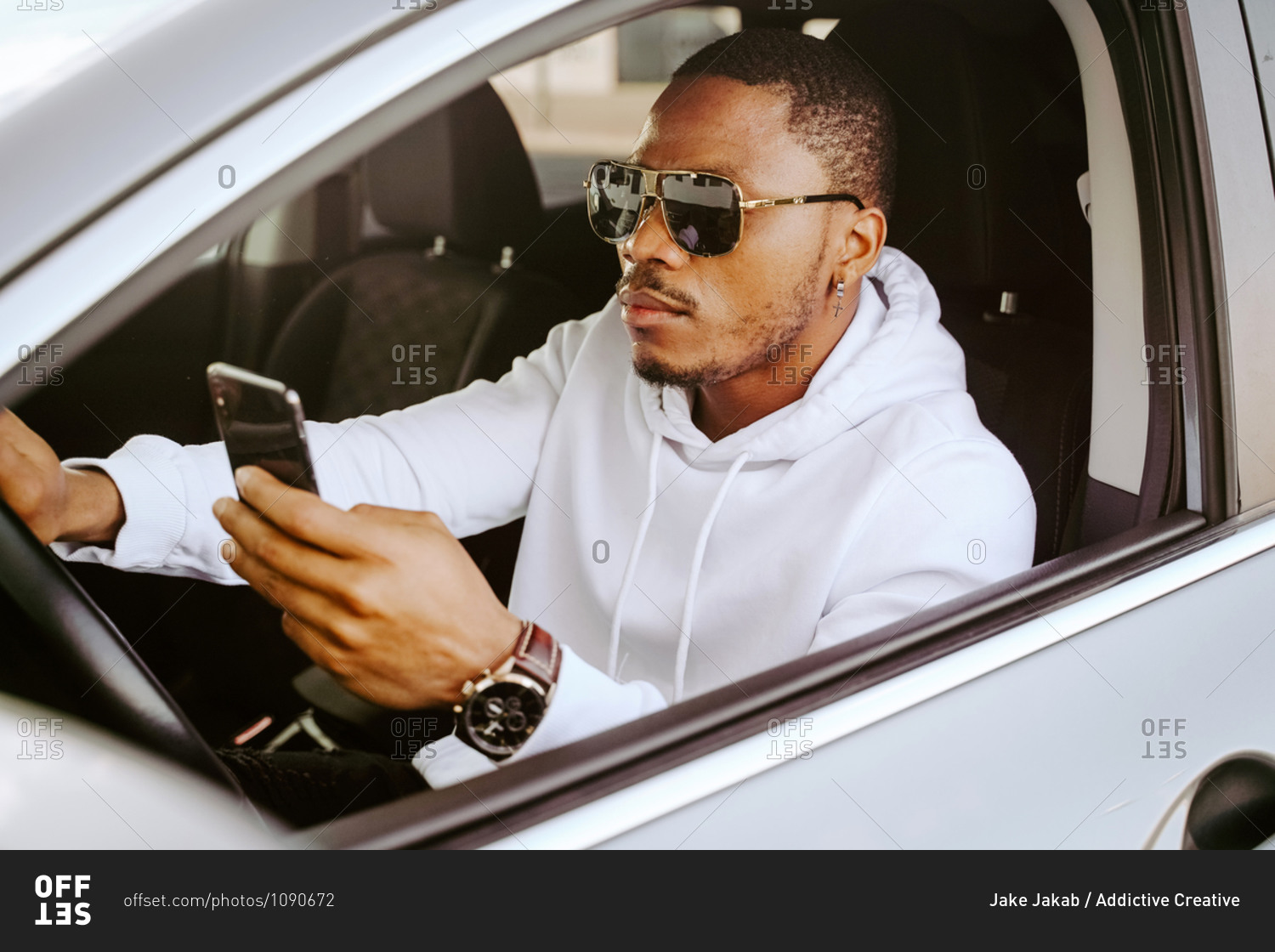 Side view of rich determined African American male driver sitting in parked car and browsing smartphone