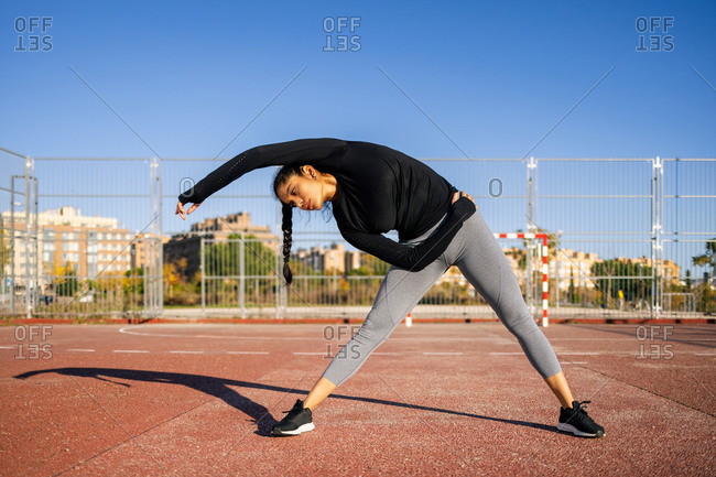 Concentrated female athlete doing stretching exercise while warming up during calisthenics training