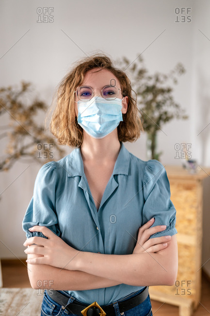 Young female with wavy hair in casual outfit and medical mask looking at camera during coronavirus