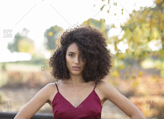 Charming African American female model with Afro hairstyle standing in autumn park and confidently looking at camera