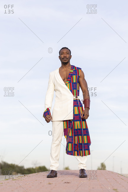 Determined African American male model in traditional costume walking on background of blue cloudy sky and looking away