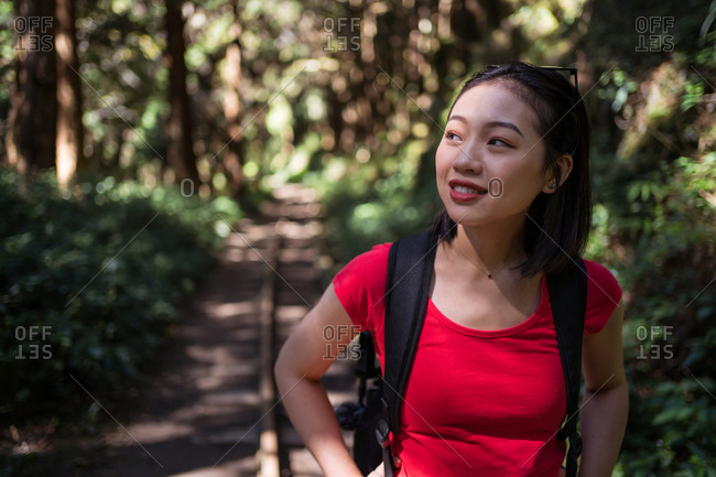 Smiling Asian female explorer with backpack standing in woods and admiring nature during summer adventure in Alishan Township