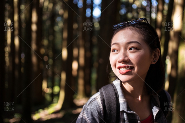 Smiling Asian female explorer with backpack standing in woods and admiring nature during summer adventure in Alishan Township