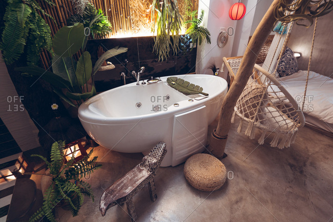 Cozy hotel room with white bathtub and hanging rope chair near green tropical plants in traditional oriental style in Taiwan